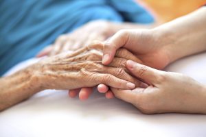 in home care services for seniors | Woman holding senior woman's hand on bed