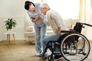 Moore Care Physical disability. Nice sad aged man holding a caregivers hand and trying to get up while having a physical disability